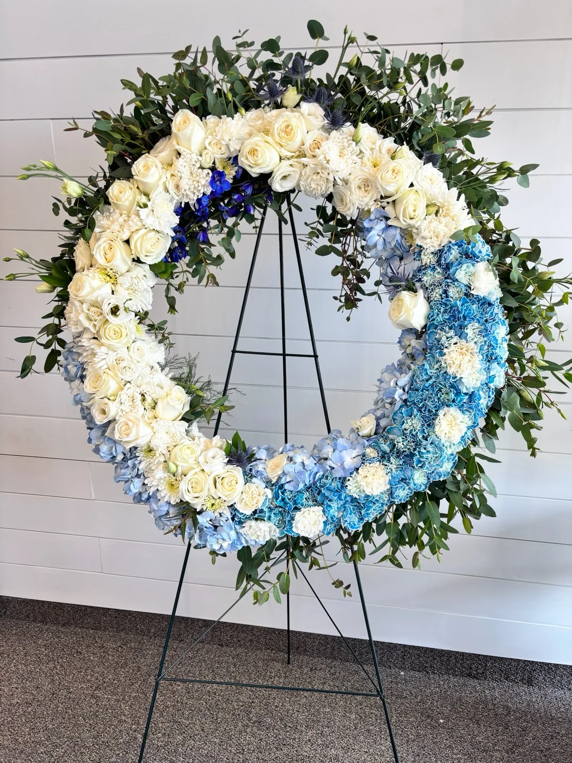 Blue and white funeral wreath on easel designed by A Ray of Sunshine Floral in Hilliard, Ohio